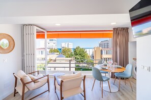 A modern hotel room with a balcony, a dining area, and a view of the cityscape.