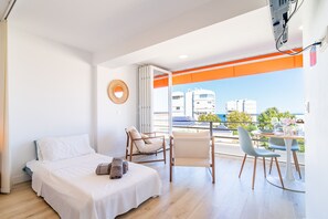 A bedroom with a bed, a chair, a table with chairs, and a view of buildings through a window.