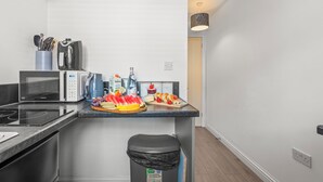 A modern kitchen with a microwave, kettle, and coffee maker. There is a trash bin and a countertop with food items. - City Centre House with EV Parking  (Coventry)
