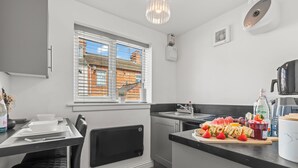 A modern kitchen with a dining area, a window with blinds, a built-in oven, and a countertop with food items. - City Centre House with EV Parking  (Coventry)