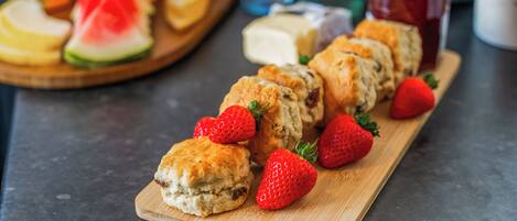A wooden board with scones and strawberries, a watermelon slice, and a glass of jam.