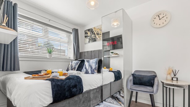 A modern bedroom with a bed, bedside table, chair, and a TV. - City Centre House with EV Parking  (Coventry)