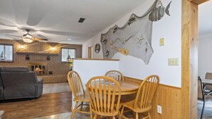 A dining area with a wooden table and chairs, a brick fireplace, and a ceiling fan.