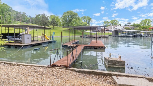 A lakeside dock area with wooden platforms, a covered seating area, and a small building with a water pump.