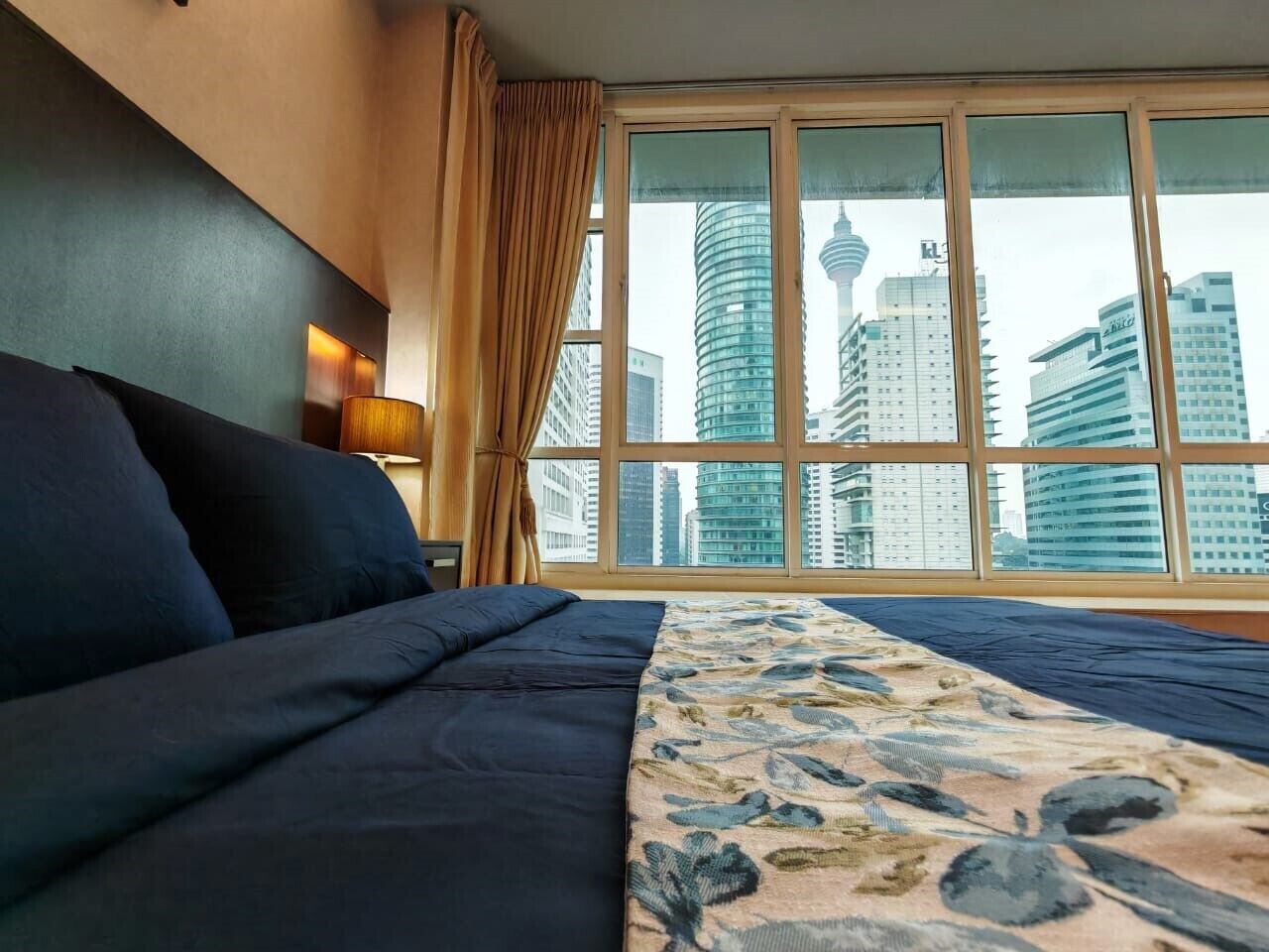Een hotelkamer met een groot bed, uitzicht op hoge gebouwen en een raam met gordijnen.
