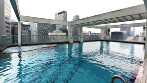 Una piscina interior con agua azul cristalina, rodeada por una estructura arquitectónica moderna con barandillas de vidrio y vistas al horizonte de la ciudad.
