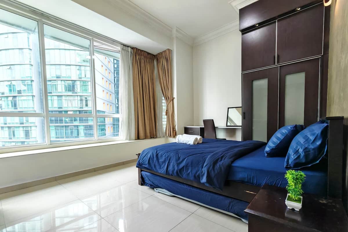 A modern bedroom with a large bed, a desk, and a view of a cityscape through floor-to-ceiling windows.