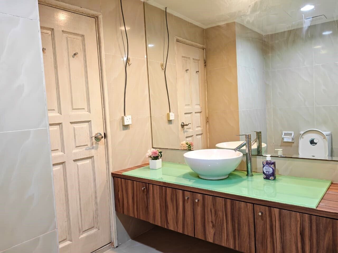 Un baño con un espejo grande, un lavamanos blanco, armarios de madera y encimera verde.