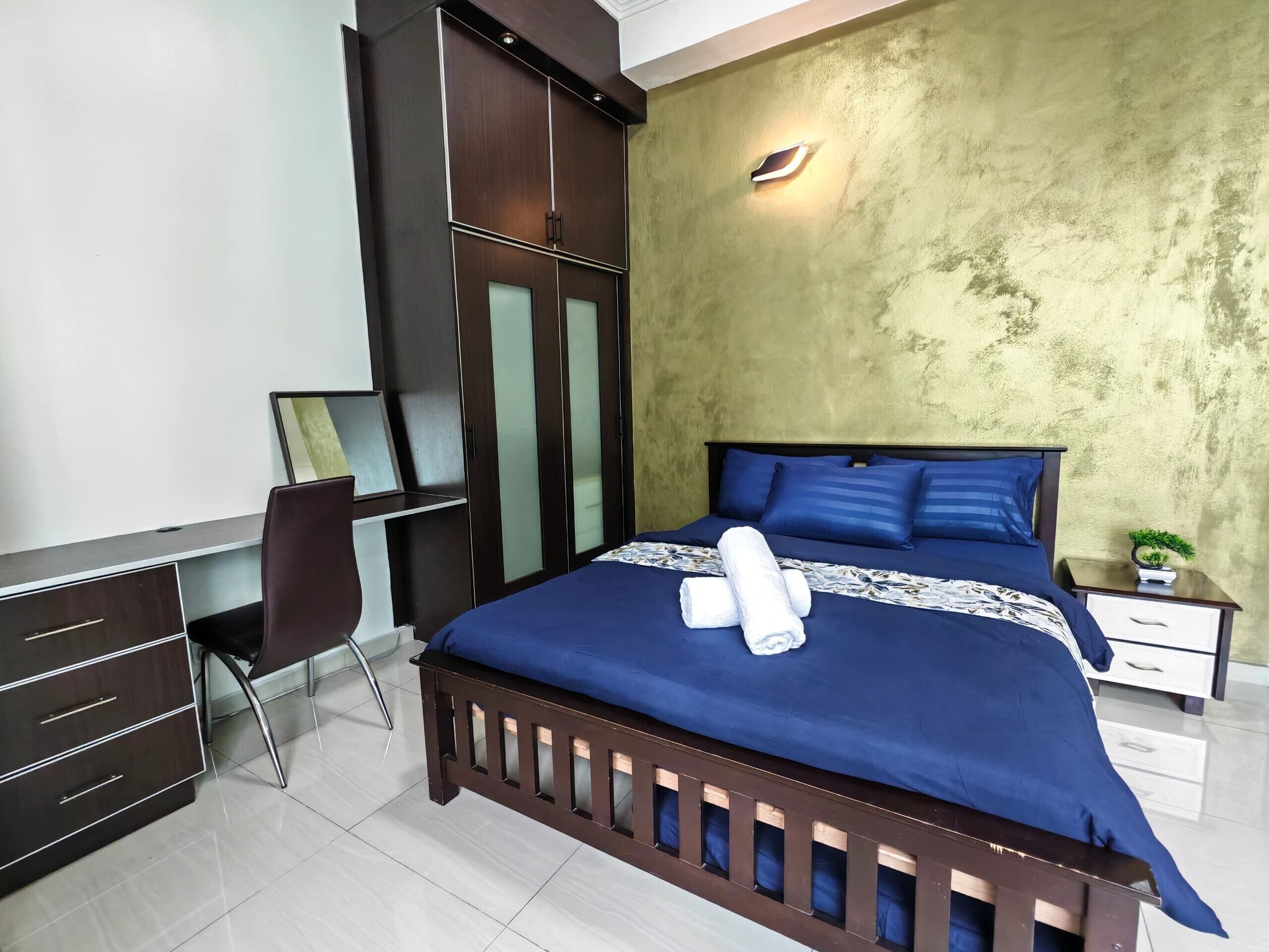 A bedroom with a bed, a desk, a chair, a wardrobe, and a nightstand with a plant.