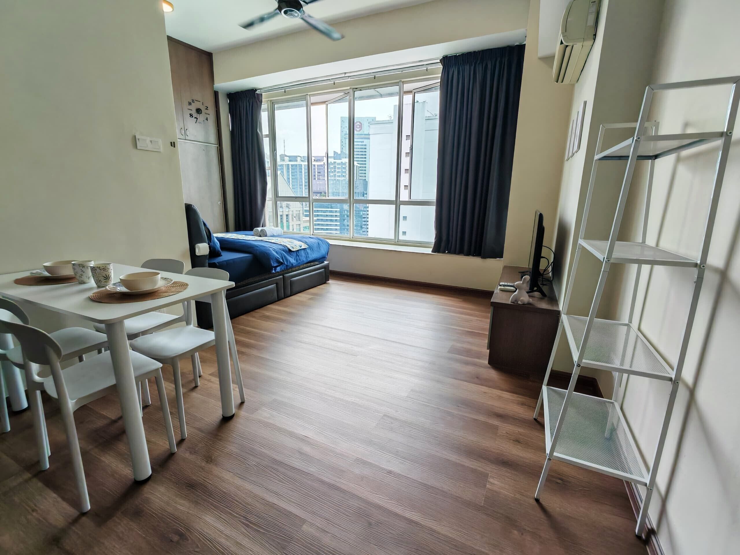A modern room with a dining table, chairs, a bed, a window with curtains, and a metal shelf unit.