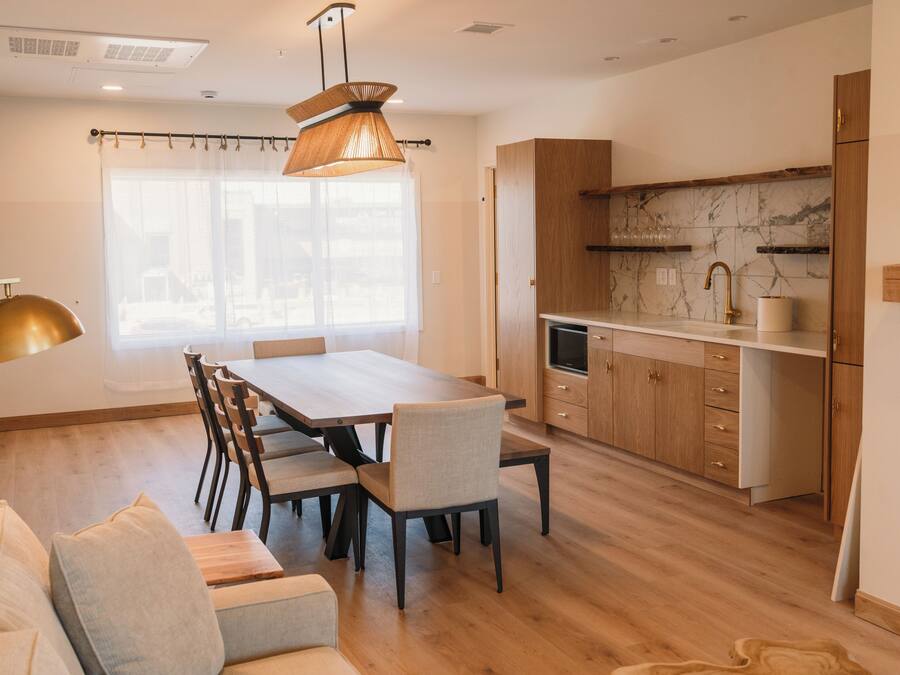 A modern kitchen with wooden cabinets, a marble backsplash, and a dining area with a wooden table and chairs.