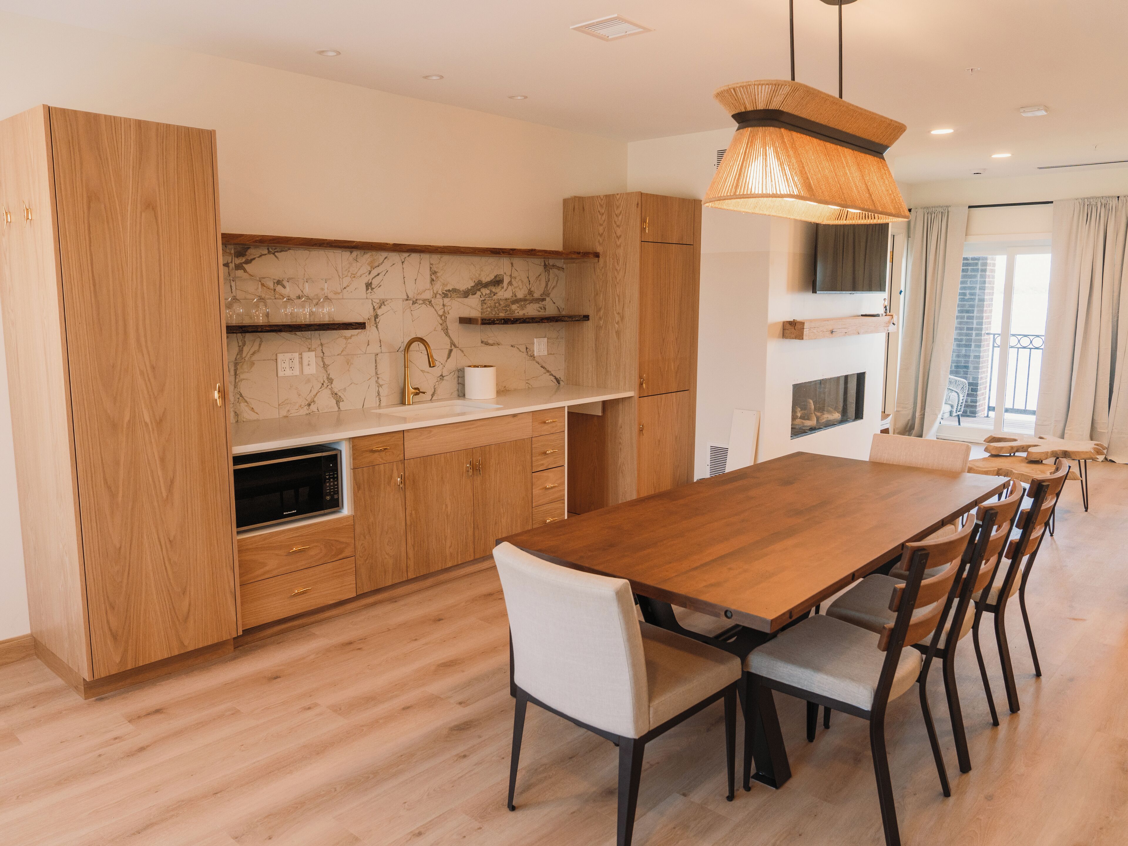 A modern kitchen with wooden cabinets, a marble backsplash, and a dining area with a wooden table and chairs.
