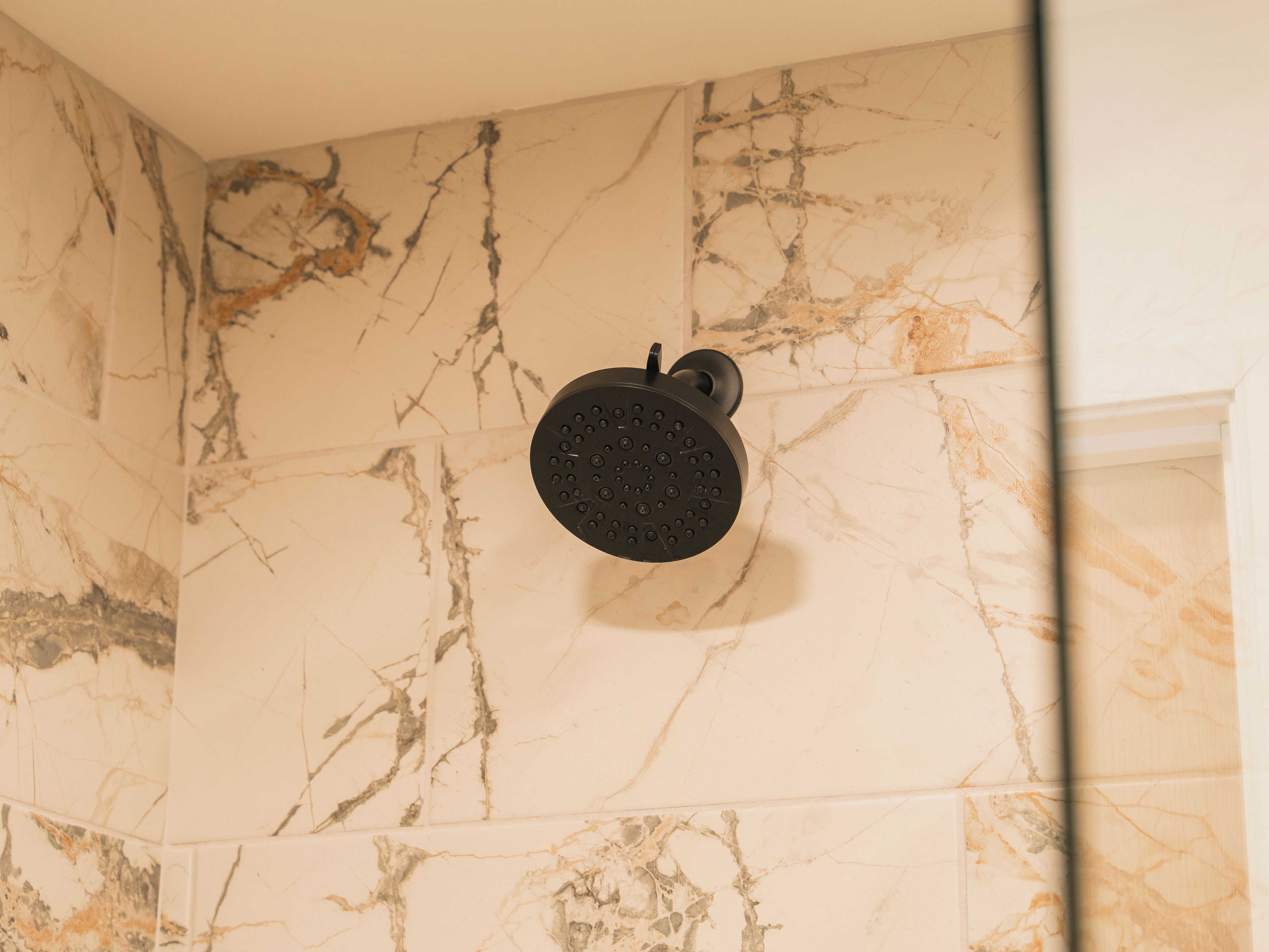 Un cabezal de ducha instalado en una pared con diseños de baldosas que imitan el mármol.