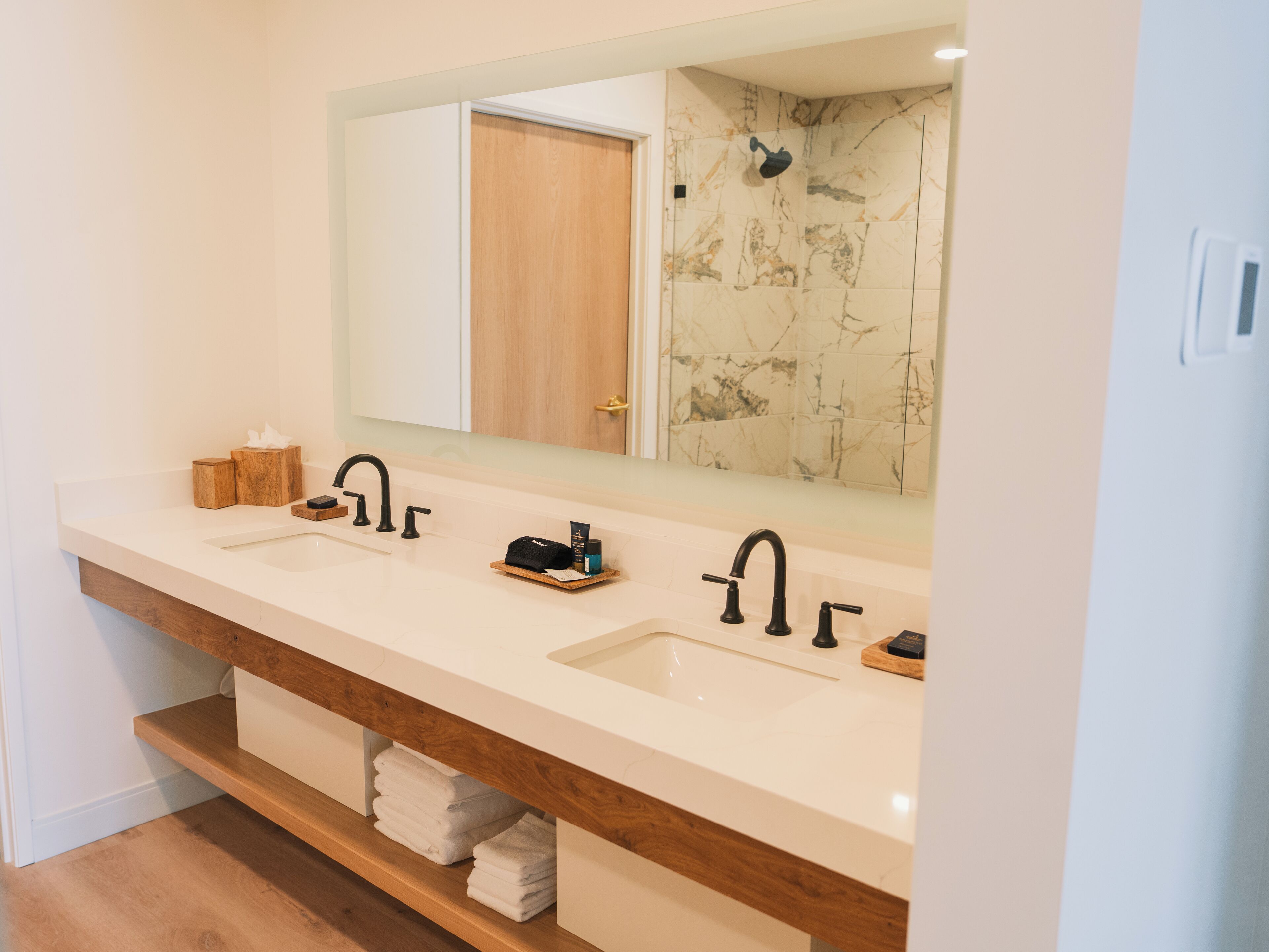 A modern bathroom with two sinks, a large mirror, and a wooden vanity.
