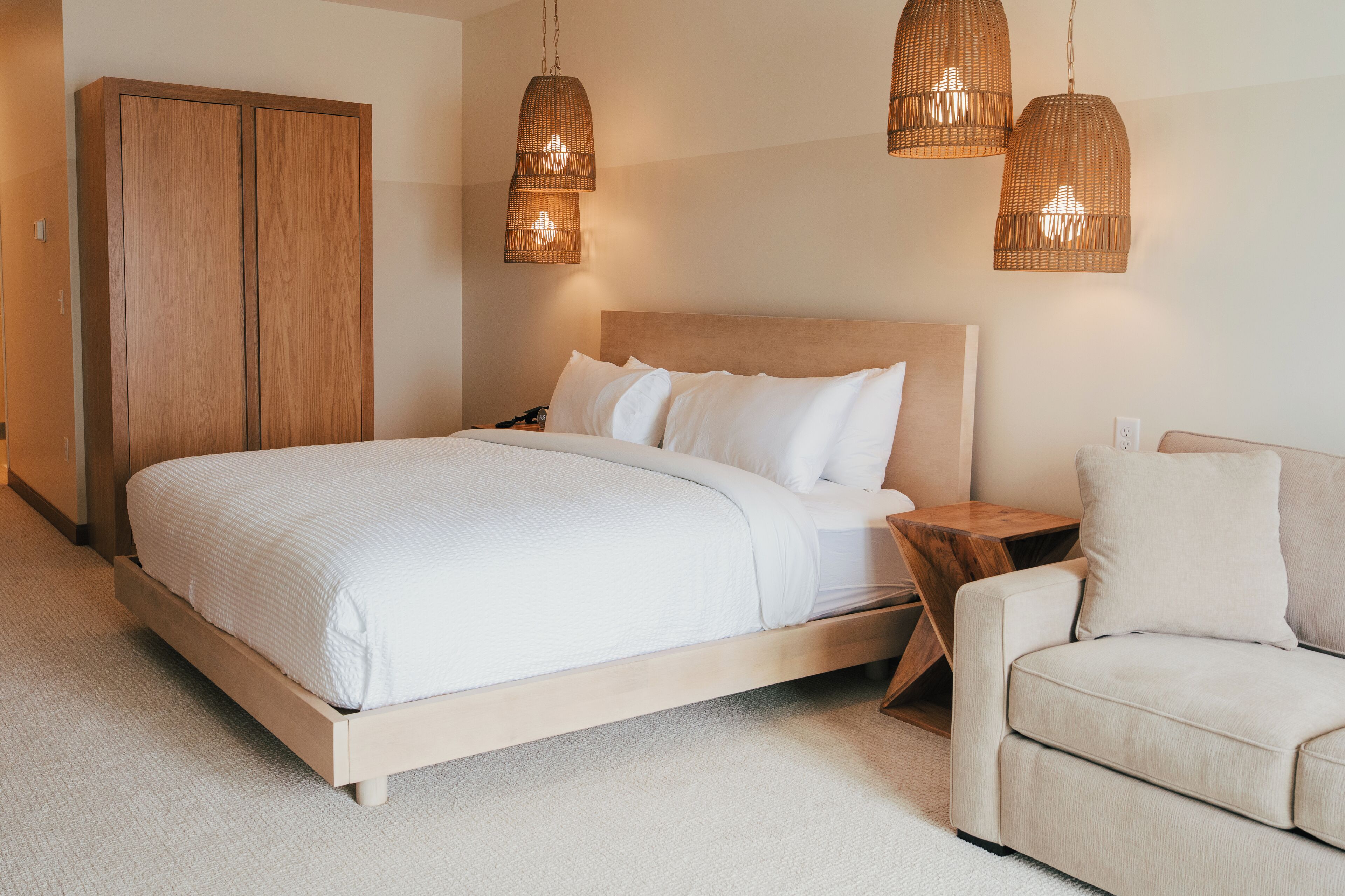A bedroom with a bed, a wooden wardrobe, a wooden nightstand, and a beige sofa.