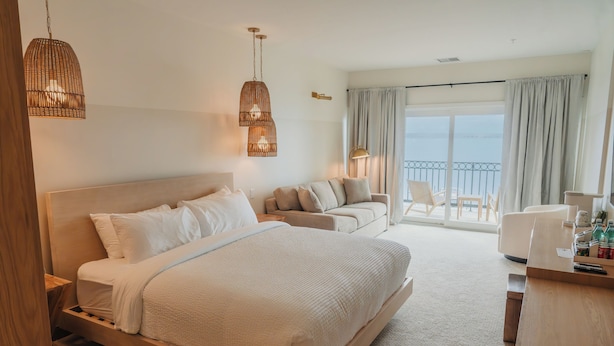 A hotel room with a bed, a sofa, a desk, and a balcony with chairs. - The Shoreline Hotel (Spring Park)