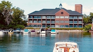 A large hotel with multiple floors and a prominent tower, situated by a calm body of water with several boats docked. - The Shoreline Hotel (Spring Park)