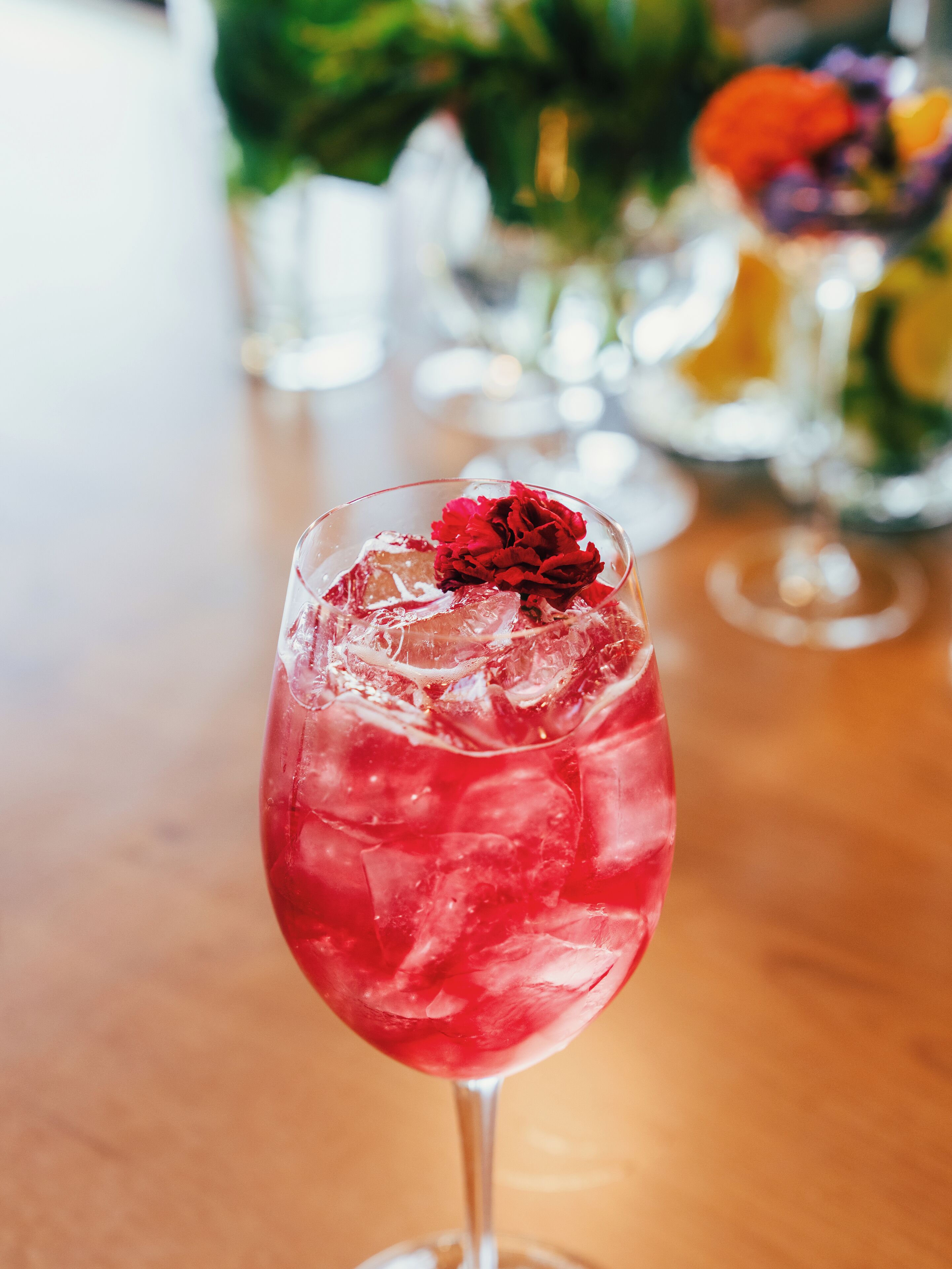 A glass with a red drink and ice cubes, placed on a wooden table.