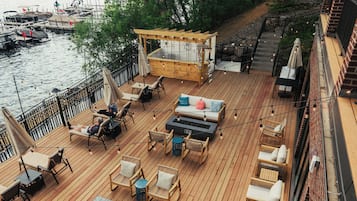 Relax on the spacious deck with lounge chairs and sofas, overlooking a serene waterfront view.