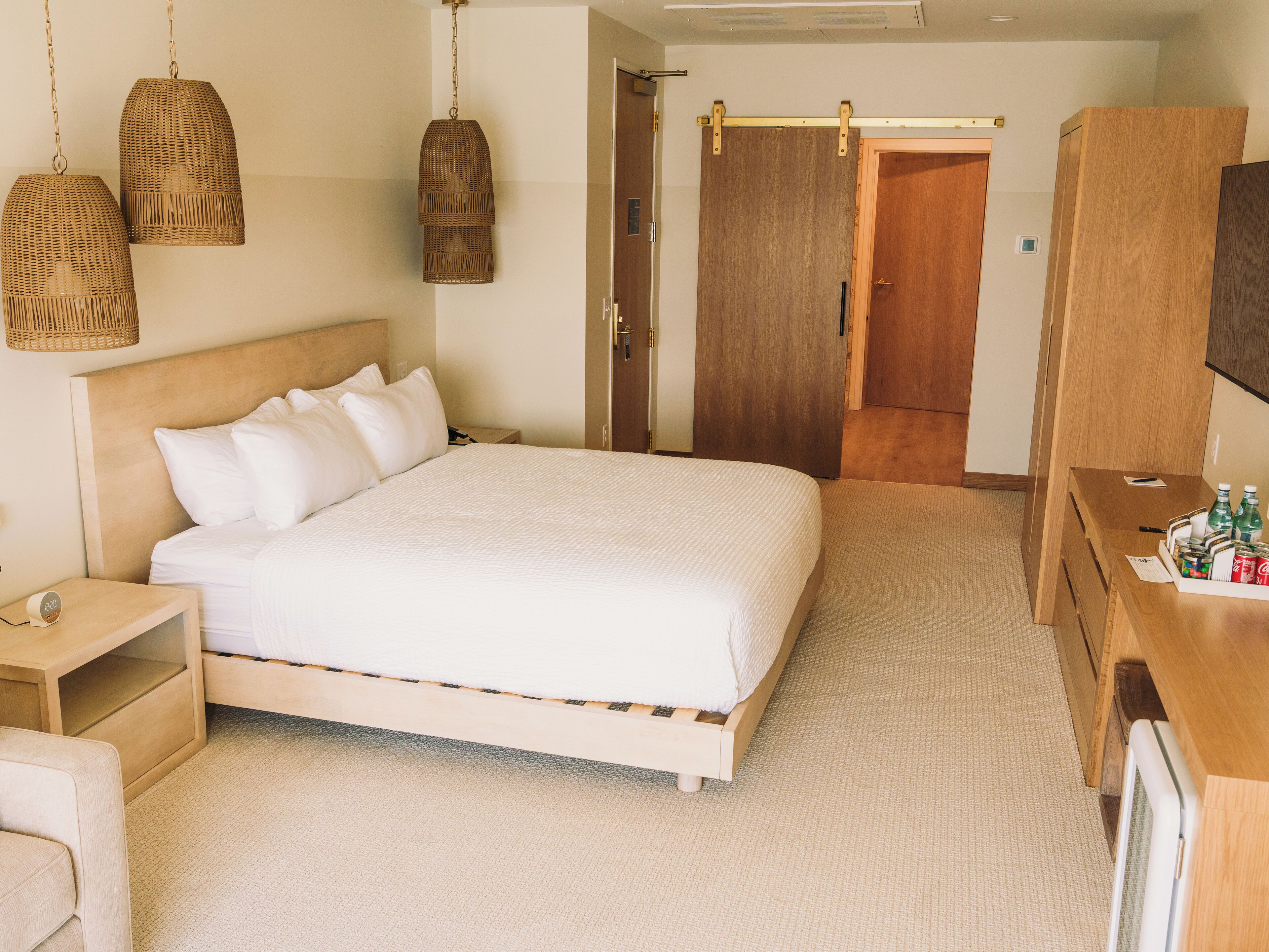 Habitación de hotel ordenada con una cama grande, mesitas de noche, un armario de madera y lámparas colgantes de mimbre.