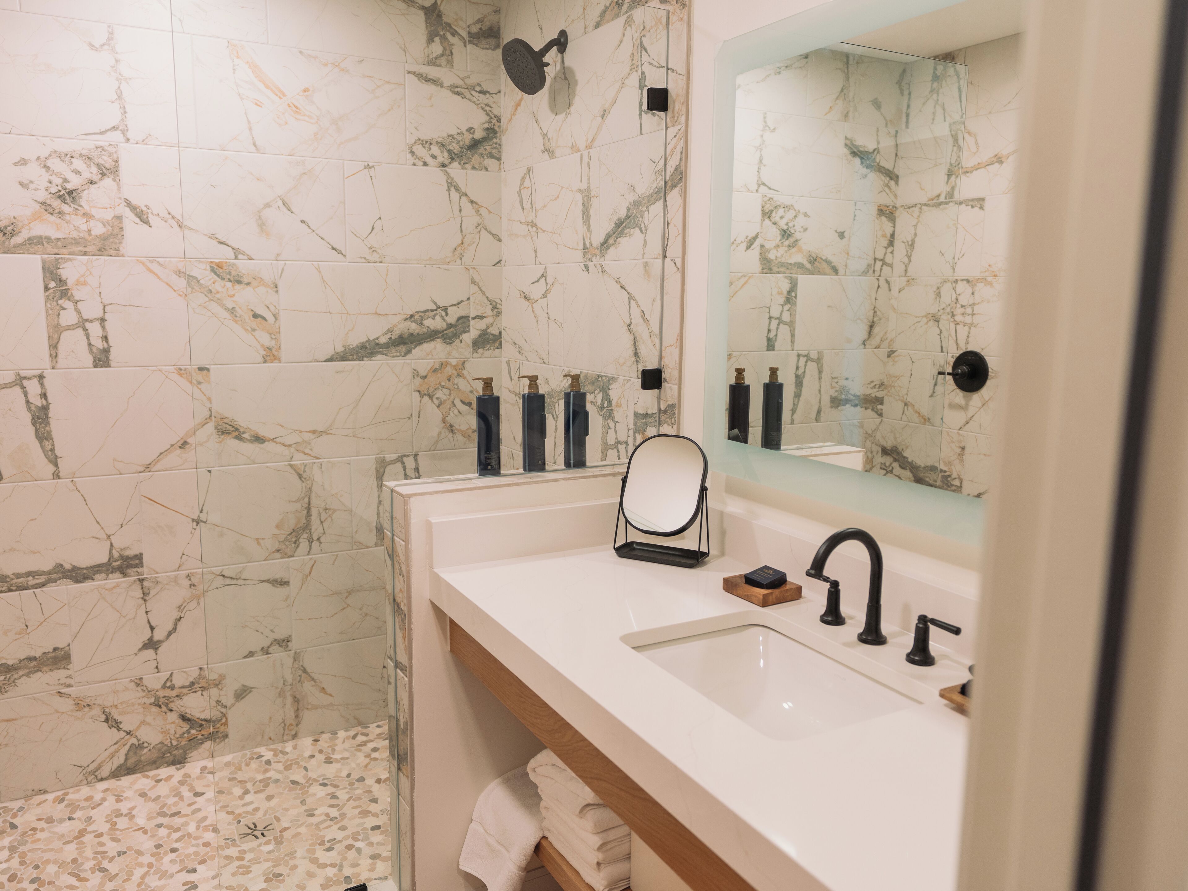 A bathroom with marble tiles, a white sink, black faucets, a mirror, and a towel rack.