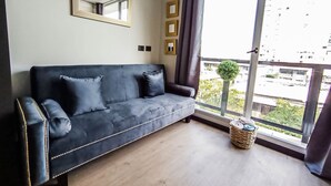 Een moderne woonkamer met een donkerblauwe bank, een groot raam met gordijnen, een spiegel en een kleine plant op de vensterbank.