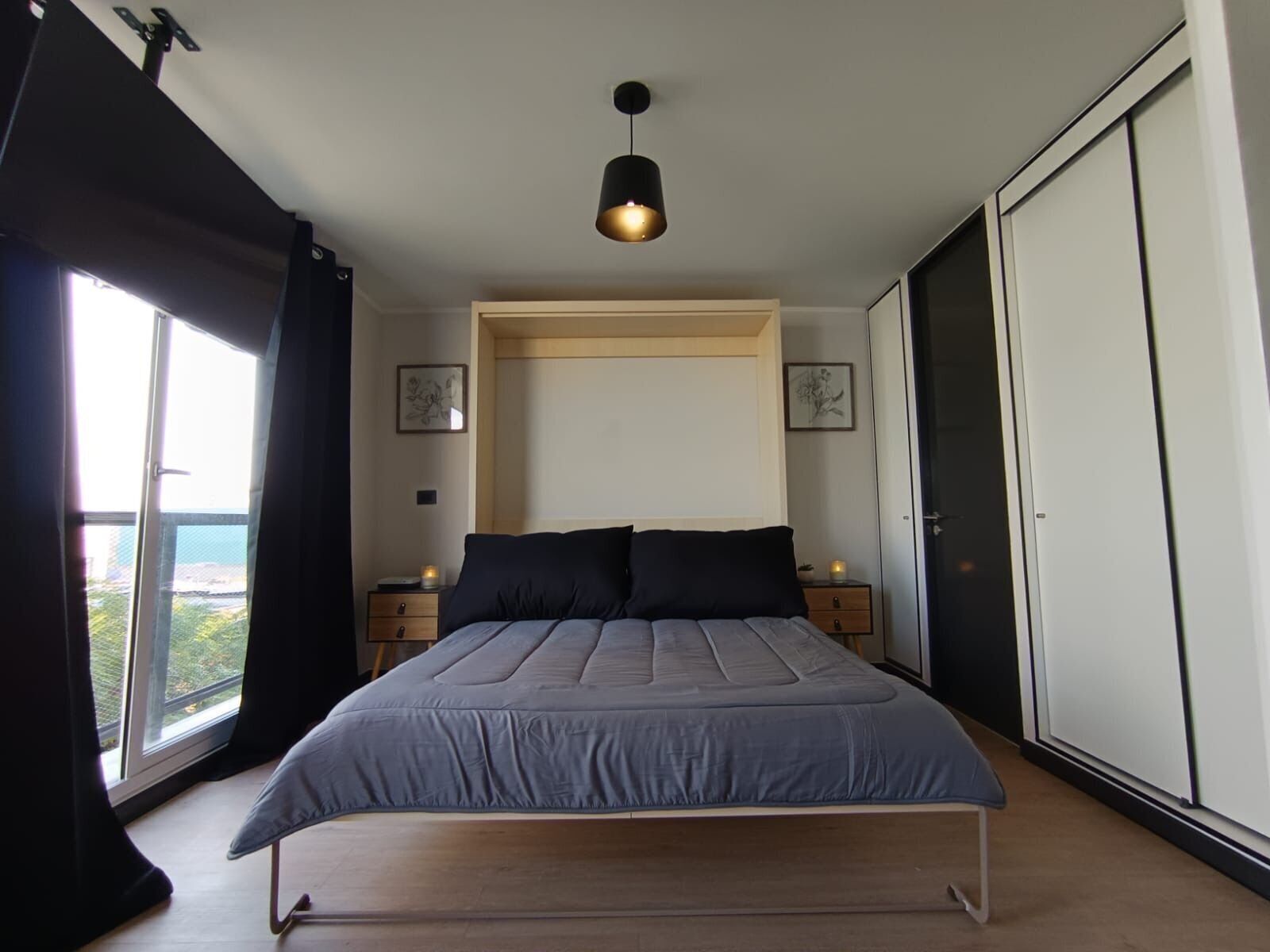Una camera da letto con un letto, comodini, un armadio, una finestra con tende e una lampada a sospensione.