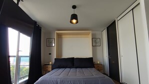 Een slaapkamer met een bed, nachtkastjes, een kledingkast, een raam met gordijnen en een hanglamp.