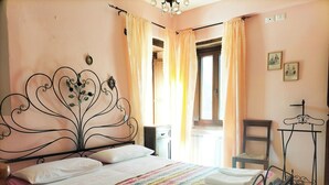 A neatly made bed with a colorful striped bedspread and white pillows, a metal headboard with floral designs, a small bedside table, and a chair with a metal frame. - Cottage on the Marche hills with swimming pool. (Marche)