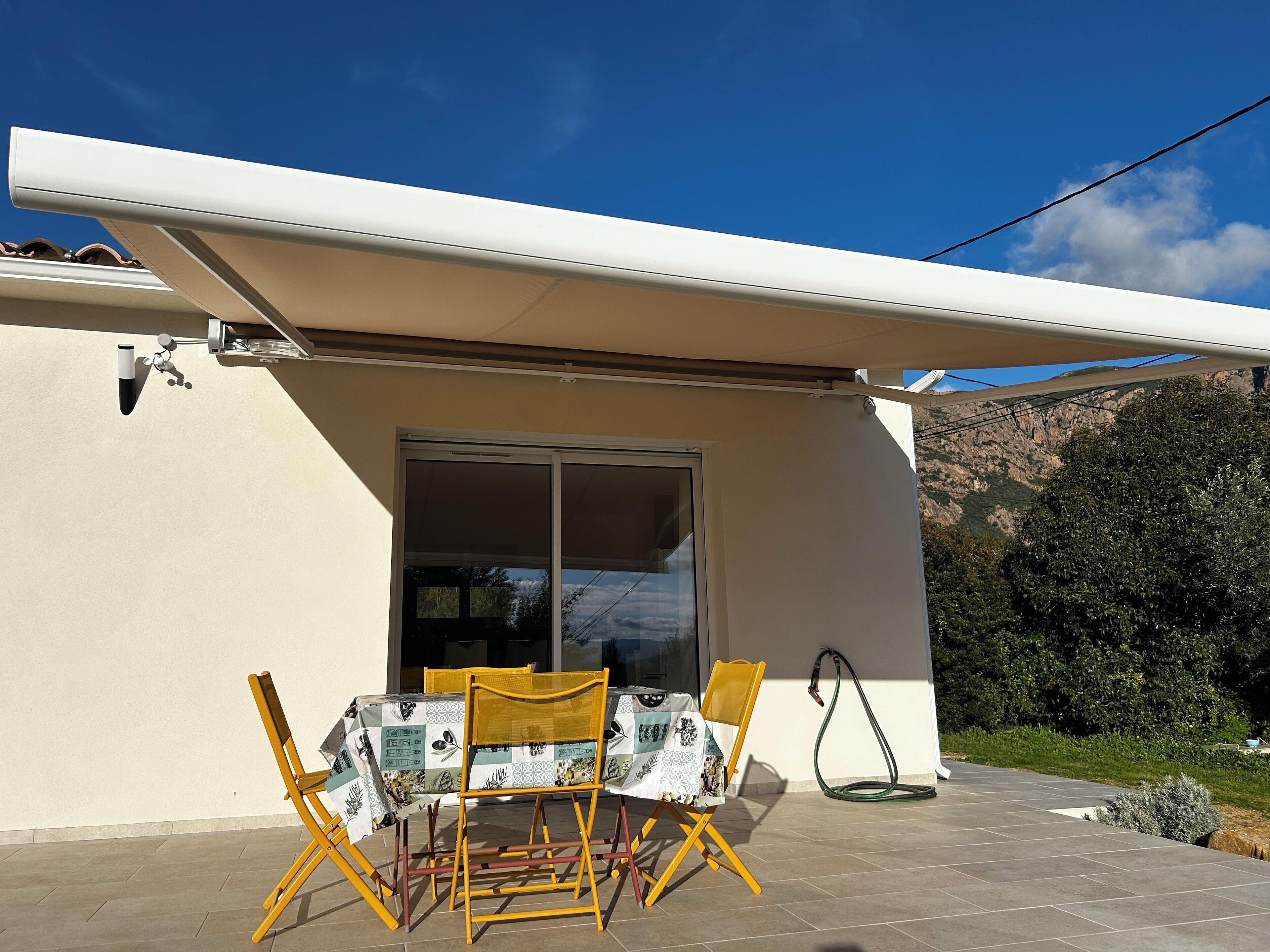 A patio with a table and chairs, a sliding glass door, and a garden hose.