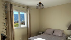A bedroom with a bed, a nightstand, a lamp, a window with curtains, and a view of the outdoors. - GITES BETWEEN SEA AND MOUNTAINS (Appietto)