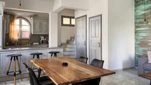 A spacious kitchen with a large island, wooden dining table, and bar stools. There is a staircase leading to an upper level. - Naxian Downtown Residence (Naxos Chora)