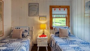 A room with two beds, a map of Maine on the wall, and a window with a view of greenery. - Charming Cottage on the Great Pond in Boothbay Harbor, Maine (Boothbay Harbor)