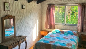 Een slaapkamer met een houten bed, een nachtkastje, een dressoir en een raam met gordijnen.