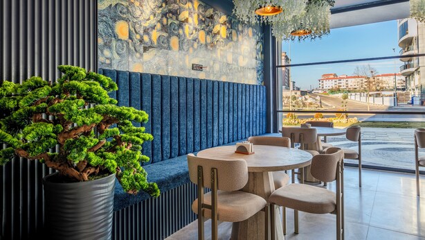 A restaurant with a blue cushioned bench seating area, a large potted bonsai tree, and a wall mural. - Dedem Hotel Premium Çorlu (Corlu)