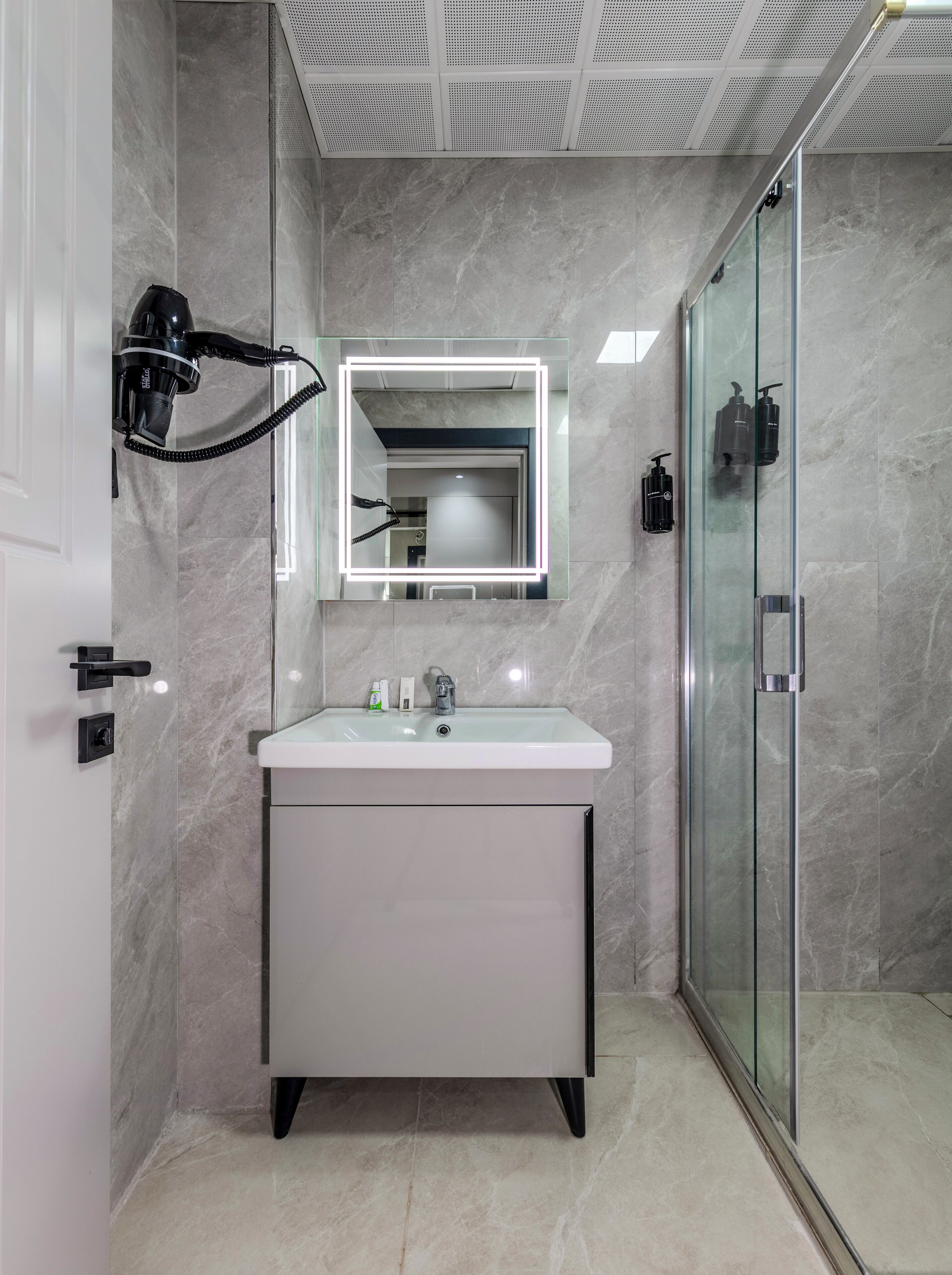 A modern bathroom with a white vanity, a glass shower enclosure, and a ceiling with a perforated design.