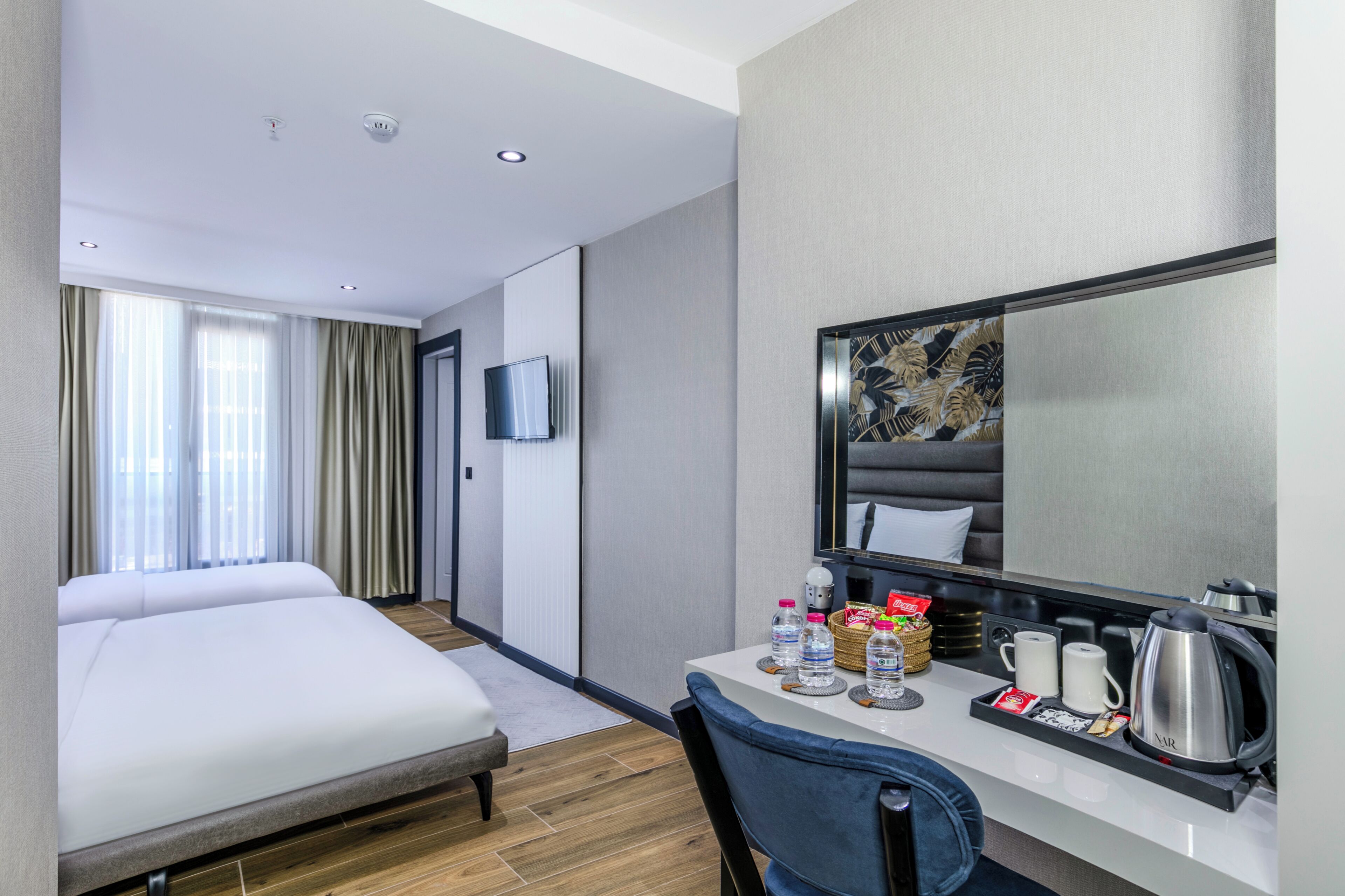 Habitación de hotel con una cama, un escritorio con cafetera, botellas de agua y un televisor.