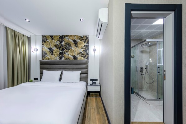 A hotel room with a bed, a nightstand, an air conditioning unit, a shower with a glass door, and a wall with a leaf-patterned design. - Dedem Hotel Premium Çorlu (Corlu)