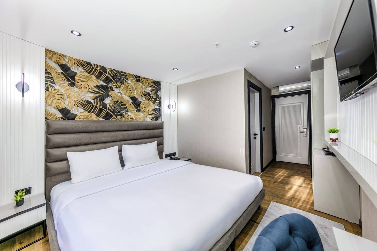 A modern hotel room with a large bed, a wall-mounted TV, and a small plant on a shelf.