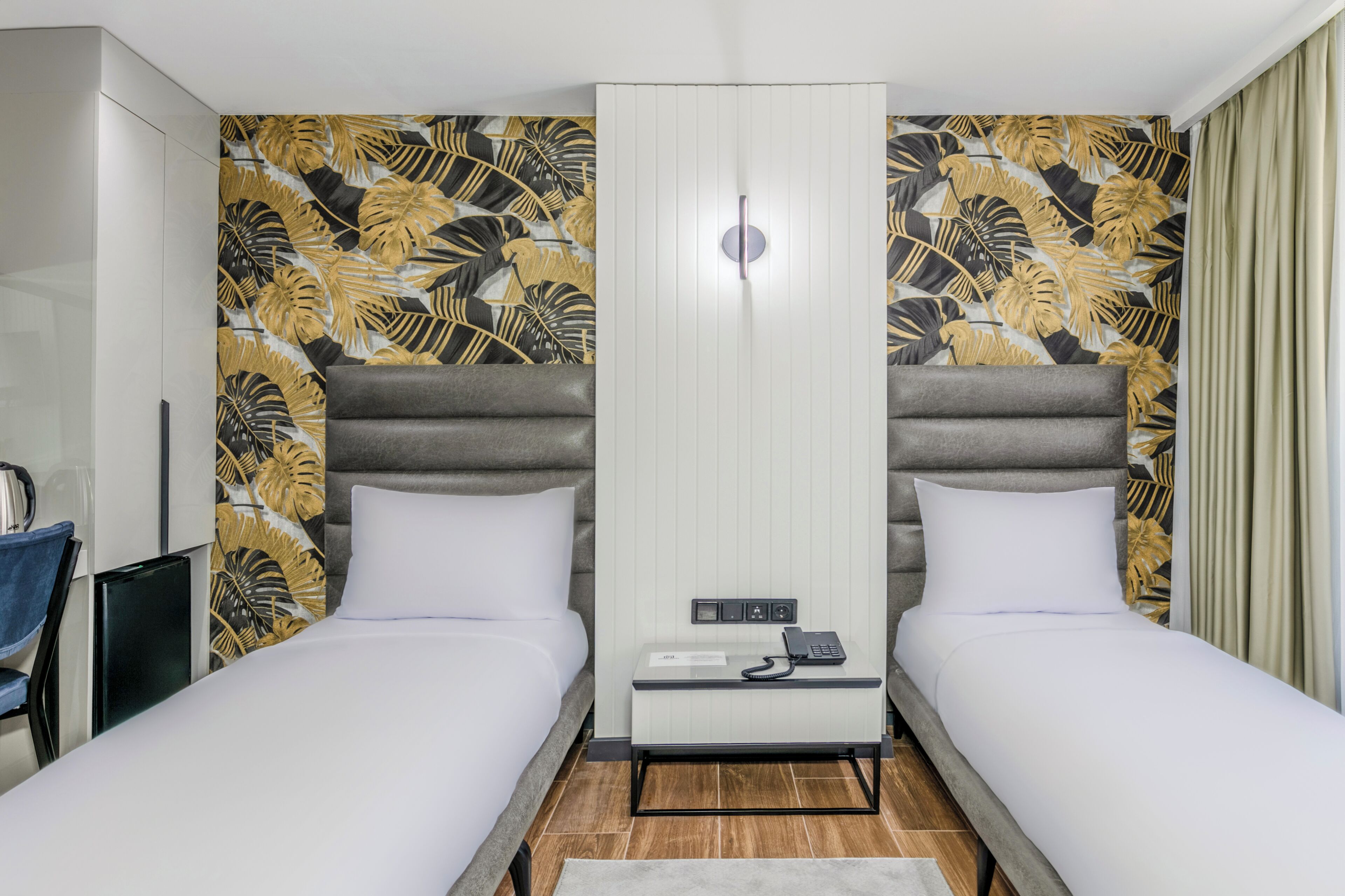 A hotel room with two beds, a minibar, and a large wardrobe.