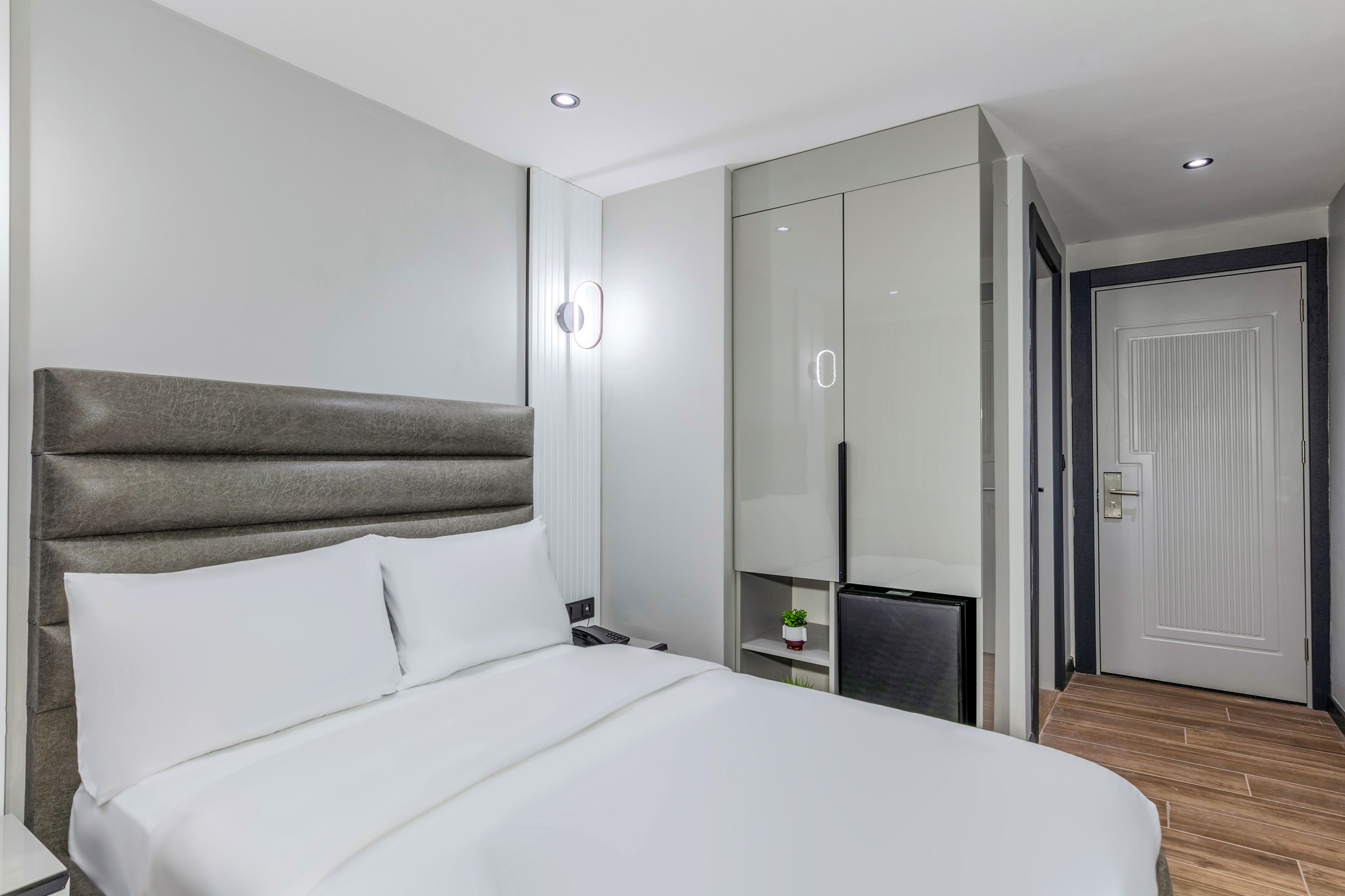 A modern hotel room with a large bed, a wardrobe, a desk, and a small plant.