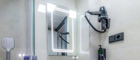 A modern bathroom with a glass-enclosed shower, a white sink, and a hairdryer mounted on the wall.