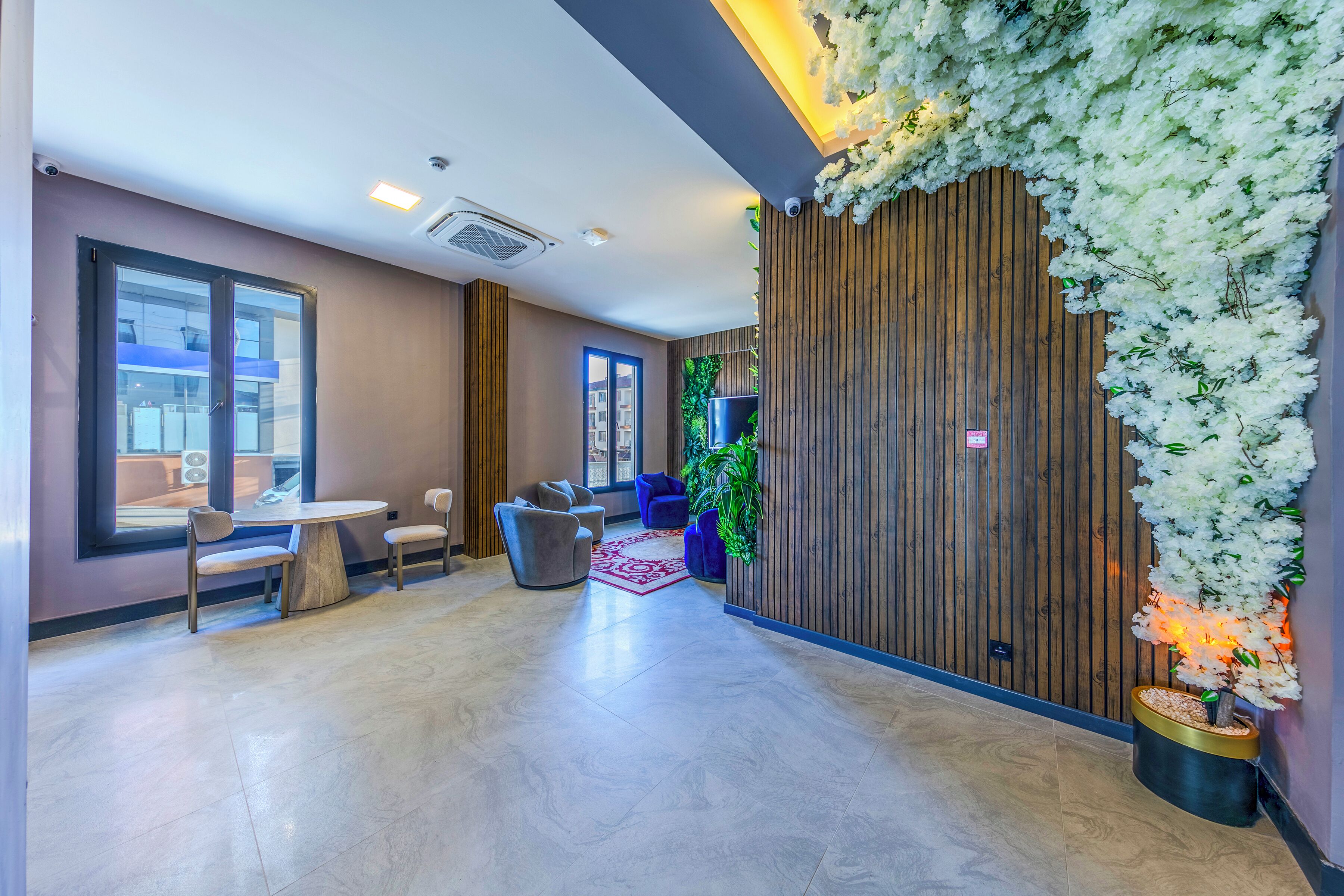 A modern lobby with a round table and chairs, a wooden accent wall, and a large window.