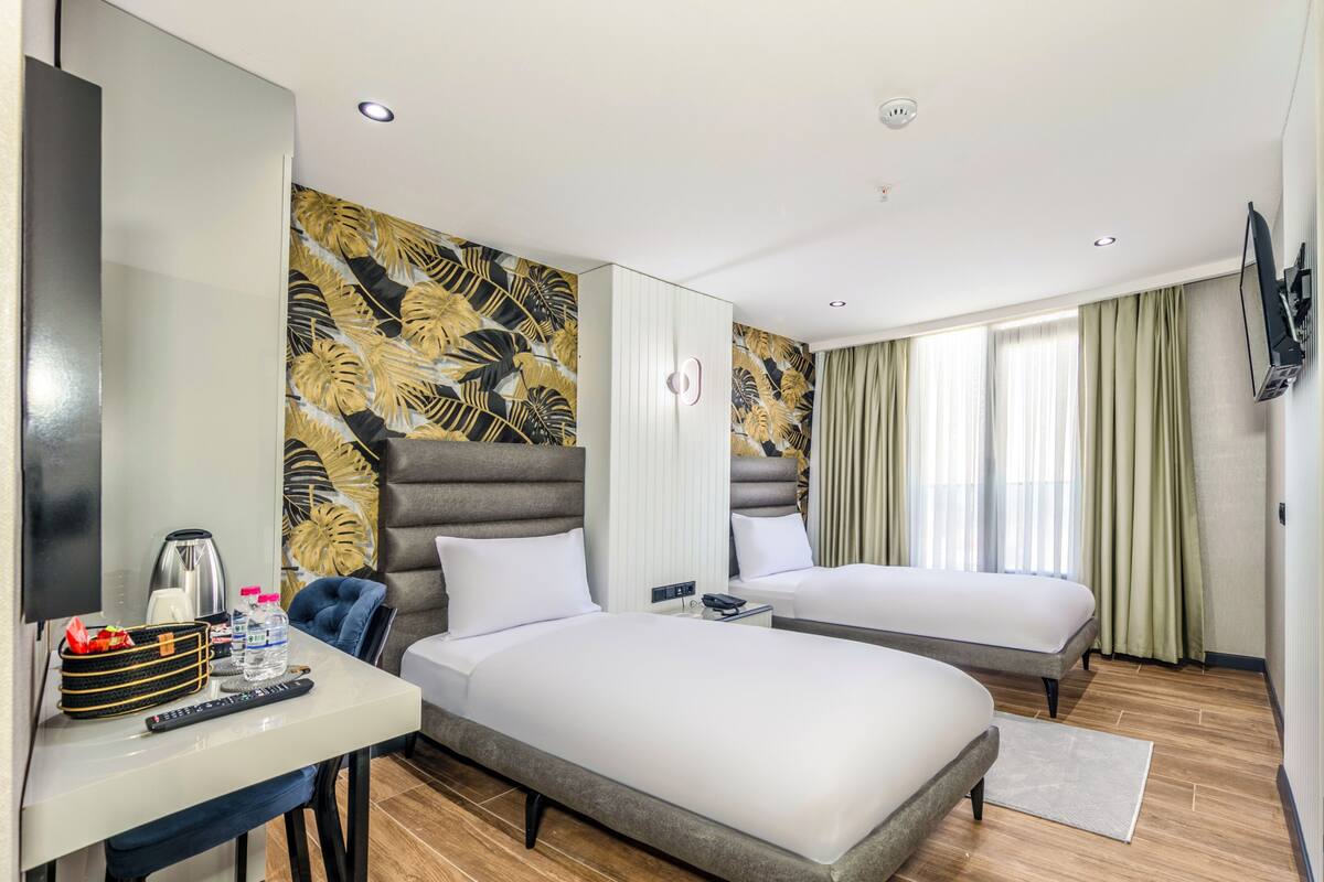 A hotel room with two beds, a desk with a chair, a television, and a large window with curtains.