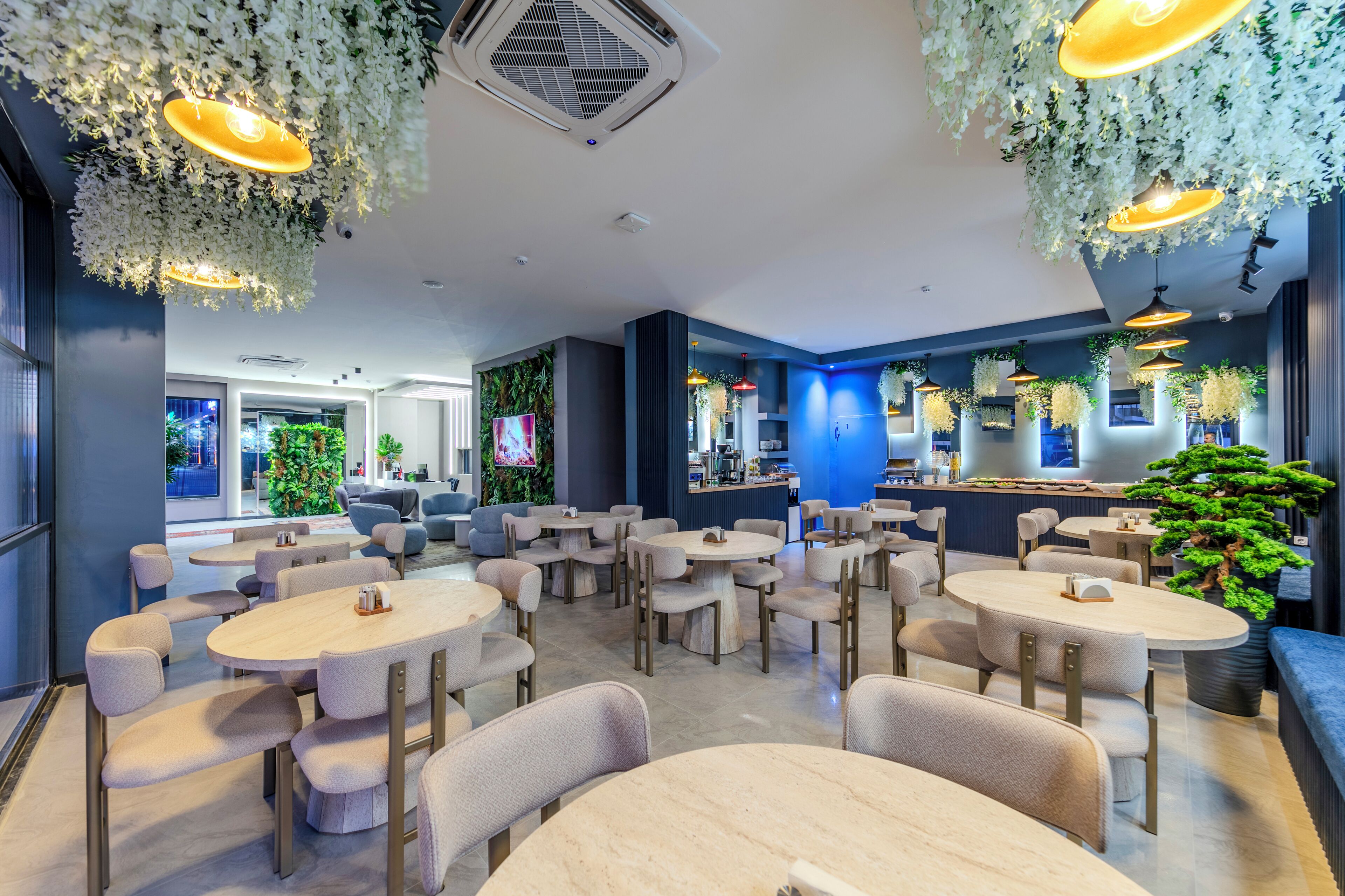 Un restaurante moderno con mesas y sillas redondas, plantas colgantes y una zona de bar.