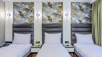 Habitación de hotel con tres camas, pared con estampado de hojas tropicales y mesitas de noche con pequeñas plantas.