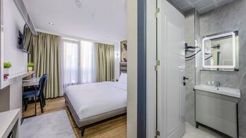 Una habitación de hotel moderna con cama, escritorio, silla y baño con espejo y lavamanos.