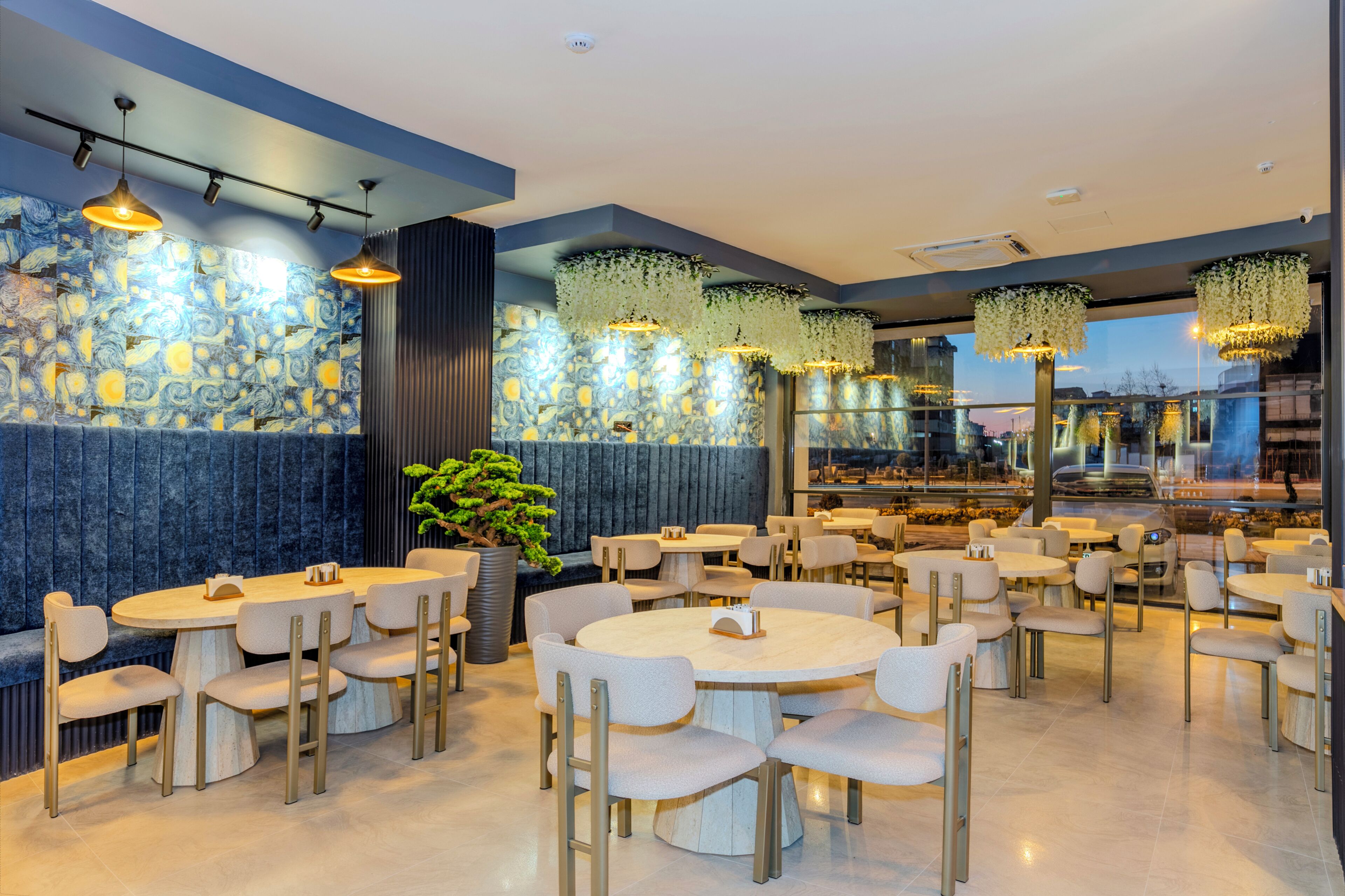 Restaurante moderno com mesas e cadeiras redondas, parede de pedra com padrão azul e luminárias florais pendentes.
