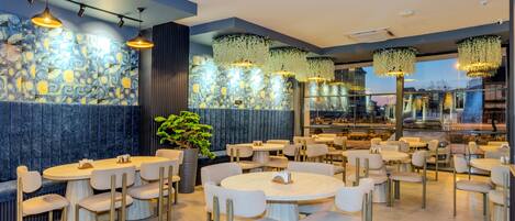 Restaurante moderno com mesas e cadeiras redondas, parede de pedra com padrão azul e luminárias florais pendentes.
