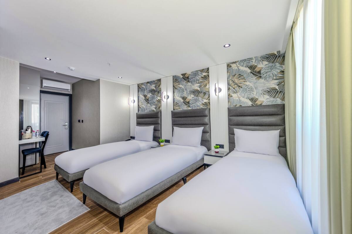 A modern hotel room with two single beds, a desk, and a vanity with a mirror.